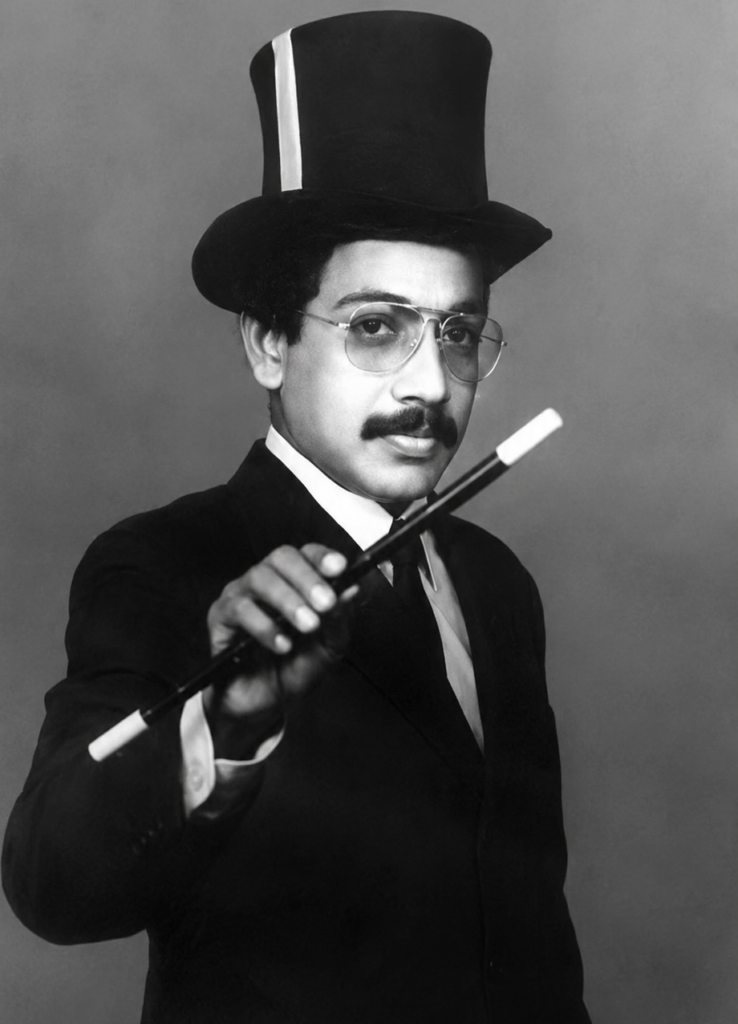 Black and white portrait of a famous magician in Kerala holding a magic wand while wearing a classic stage costume and top hat.